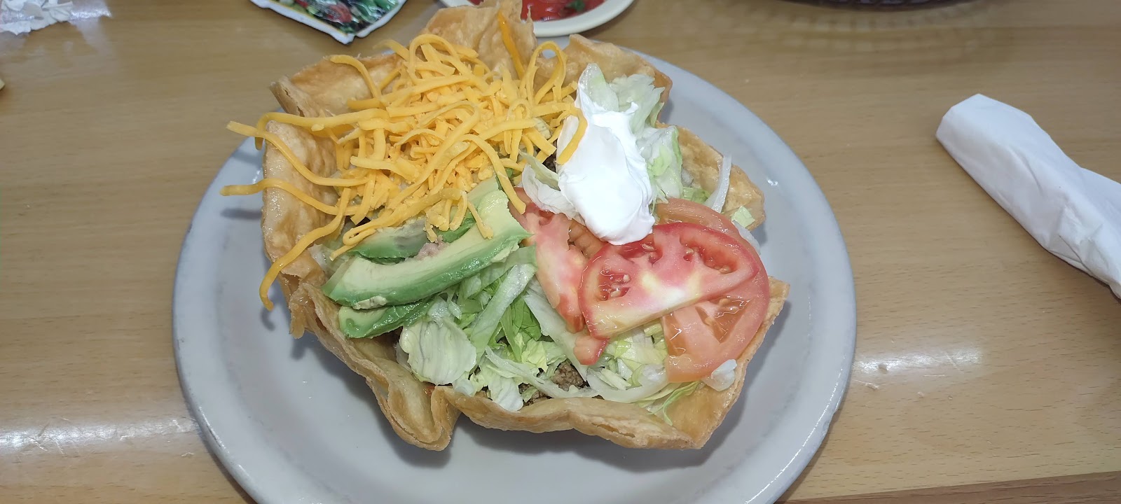 Puffy taco salad topped with cheese, avocado, tomato and sour cream